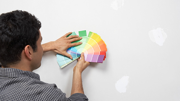 Man holding paint colour samples against interior wall